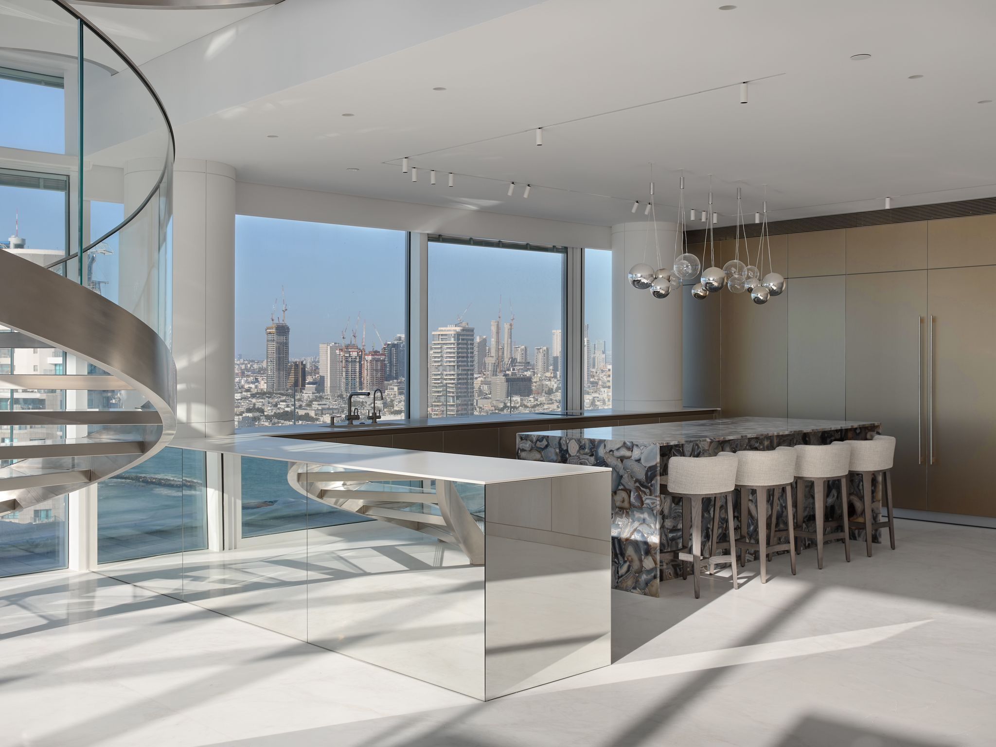 A kitchen with a island with a sitting bar, there is a glimpse of a large staircases on the left. 